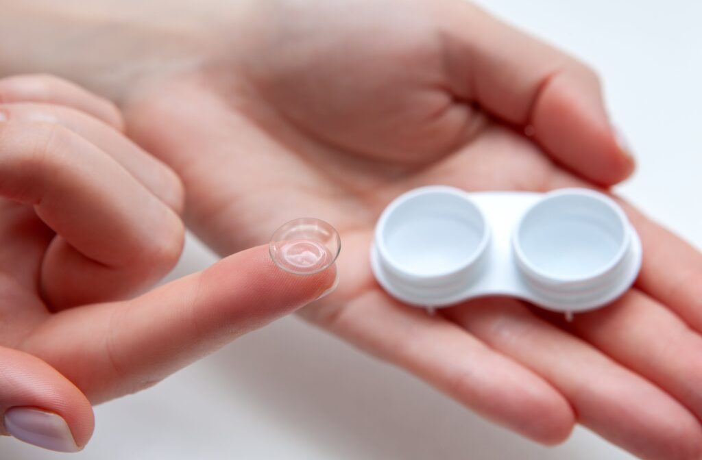 A zoomed-in image of a contact lens on the tip of a person's index finger in front of a small mirror.