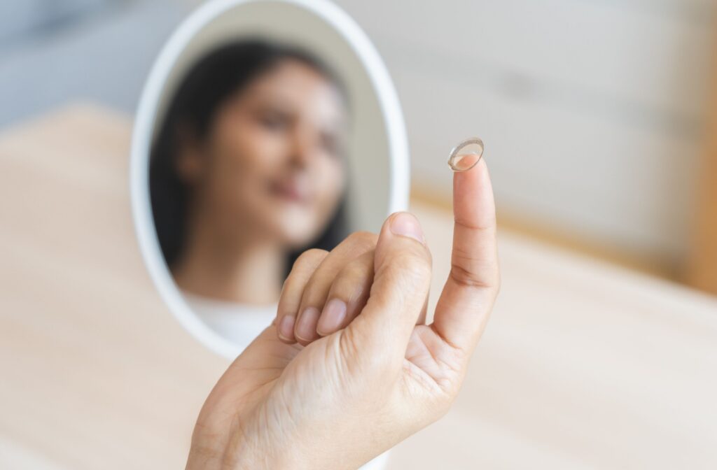 A zoomed-in image of a contact lens on the tip of a person's index finger in front of a small mirror.