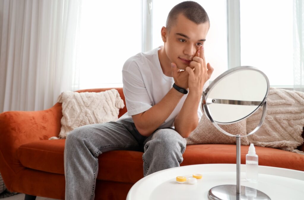 A contact lens wearer sitting on the couch and using a small mirror to put in their contact lenses.