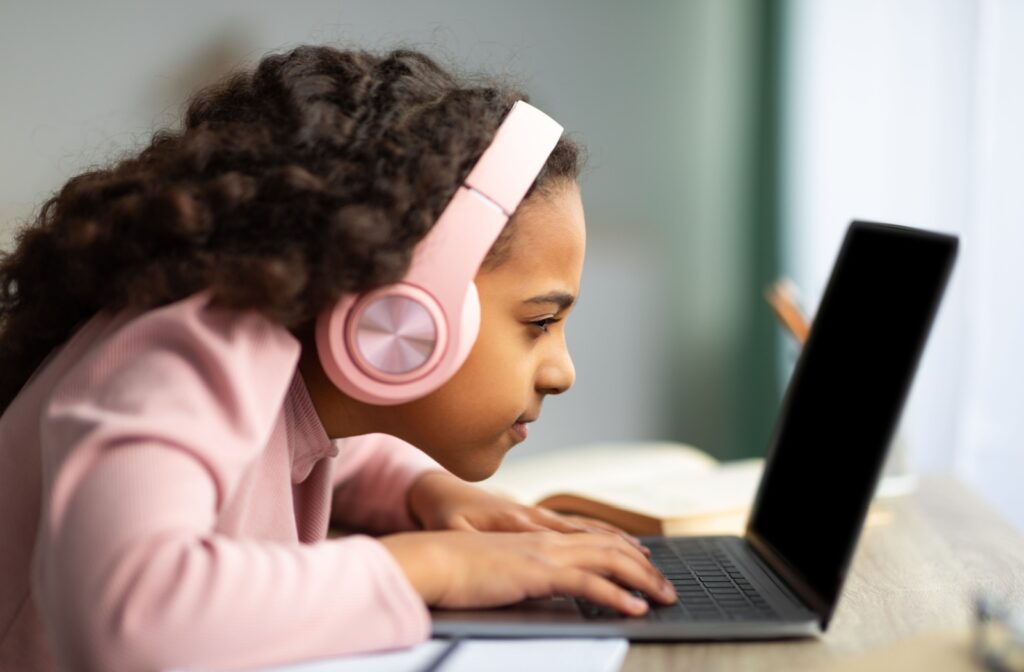 A child struggling with myopia squinting while looking close to their computer screen trying to read.