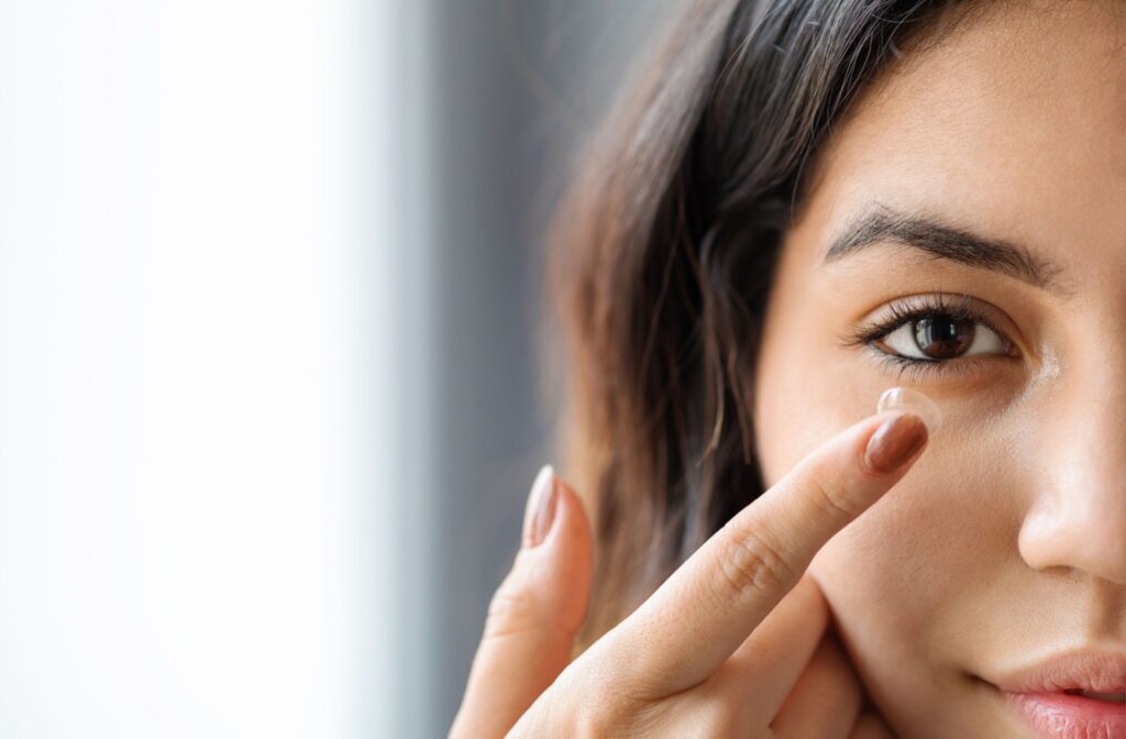Close up shot of a young adult woman putting in a contact lens in her right eye.
