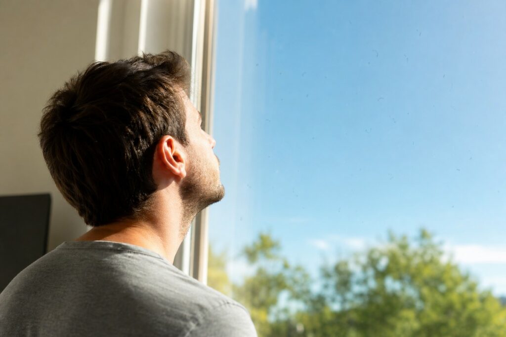 Person looking out a window at blue sky and trees.